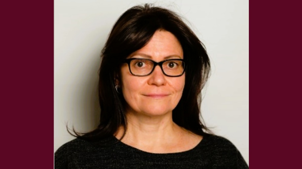 Woman with dark hair and glasses against a plain background.